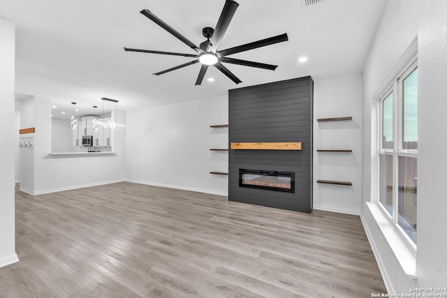 unfurnished living room with ceiling fan, a large fireplace, and light wood-type flooring