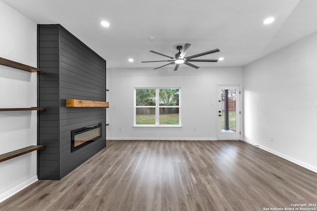 unfurnished living room featuring ceiling fan, a large fireplace, and wood-type flooring