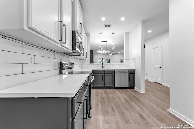 kitchen with hanging light fixtures, light hardwood / wood-style flooring, kitchen peninsula, gray cabinets, and appliances with stainless steel finishes