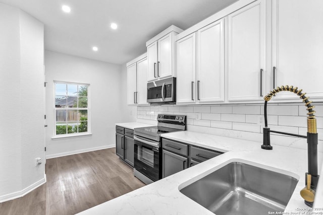 kitchen featuring light stone counters, stainless steel appliances, sink, wood-type flooring, and white cabinets