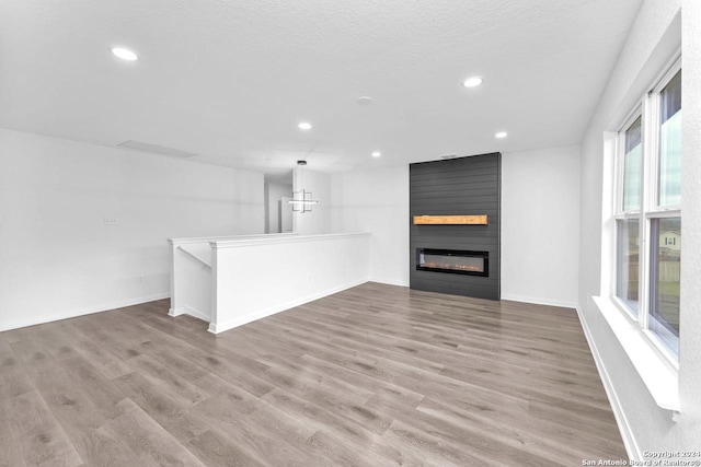 unfurnished living room featuring a fireplace, a textured ceiling, light hardwood / wood-style flooring, and a notable chandelier