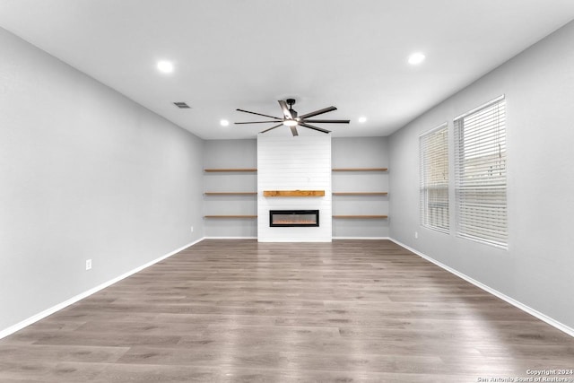 unfurnished living room featuring wood-type flooring, a large fireplace, and ceiling fan