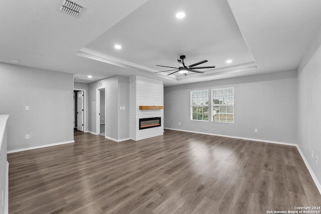 unfurnished living room featuring a large fireplace, dark hardwood / wood-style floors, a raised ceiling, and ceiling fan