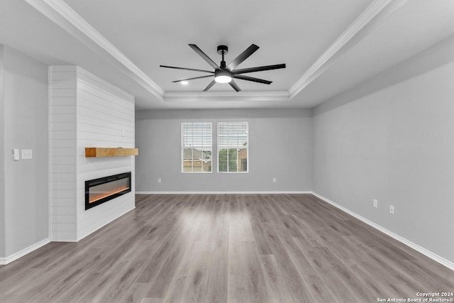 unfurnished living room with ceiling fan, ornamental molding, light wood-type flooring, a fireplace, and a tray ceiling