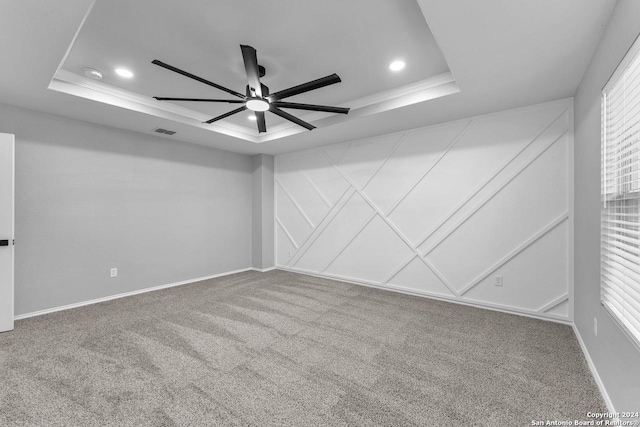 empty room with a tray ceiling, ceiling fan, and carpet floors