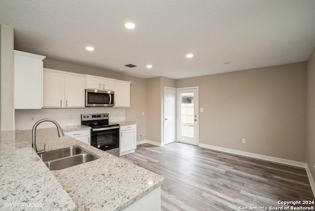 kitchen with appliances with stainless steel finishes, light stone counters, sink, white cabinets, and light hardwood / wood-style floors