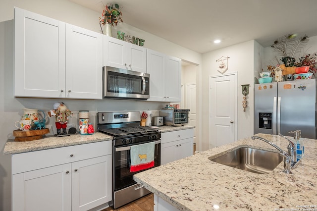 kitchen featuring light stone countertops, stainless steel appliances, sink, white cabinets, and light hardwood / wood-style floors