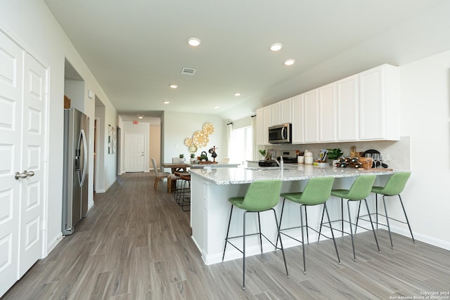 kitchen featuring a breakfast bar, white cabinetry, stainless steel appliances, kitchen peninsula, and light stone countertops