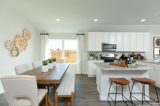 kitchen featuring appliances with stainless steel finishes, a center island, white cabinetry, dark hardwood / wood-style flooring, and light stone countertops