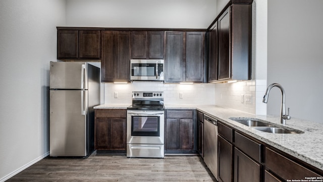 kitchen featuring sink, stainless steel appliances, light stone counters, light hardwood / wood-style floors, and dark brown cabinets