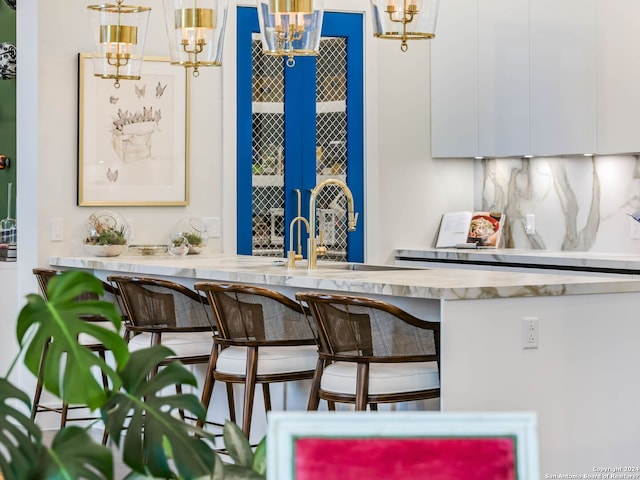 bar featuring decorative backsplash, sink, white cabinetry, and hanging light fixtures