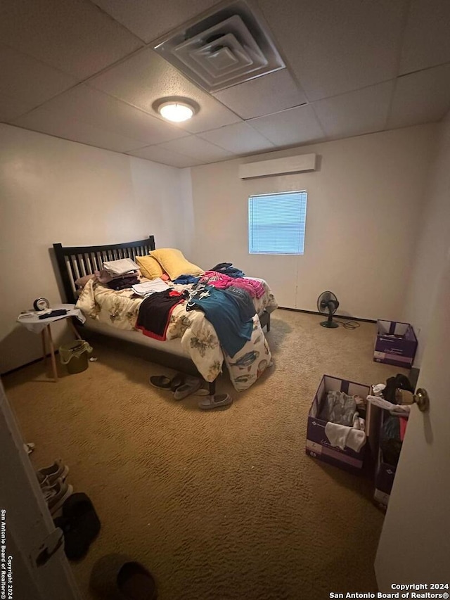 carpeted bedroom featuring a wall unit AC and a paneled ceiling