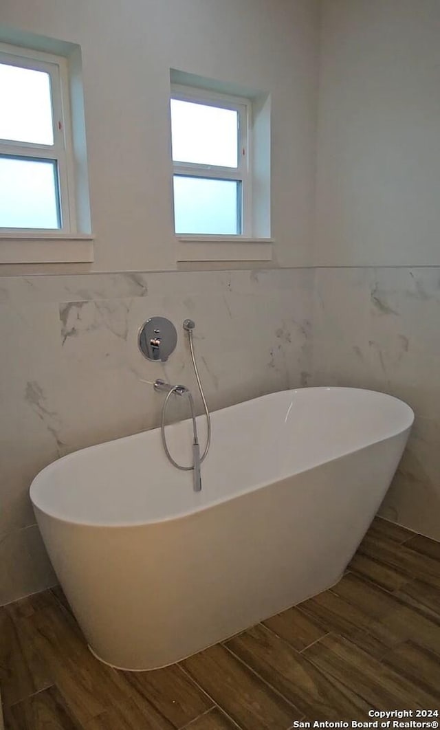 bathroom featuring hardwood / wood-style floors, a tub to relax in, and tile walls