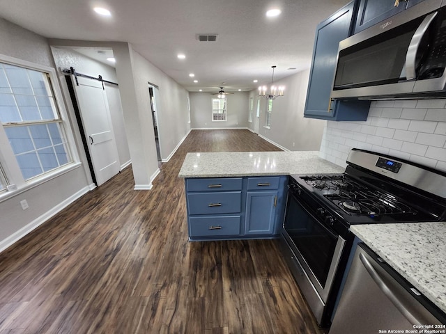 kitchen with a barn door, appliances with stainless steel finishes, kitchen peninsula, backsplash, and ceiling fan with notable chandelier