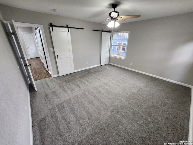 unfurnished bedroom with ceiling fan, a barn door, and dark carpet