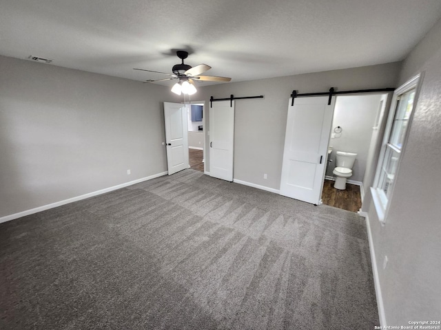 unfurnished bedroom featuring ensuite bath, multiple windows, a barn door, carpet flooring, and ceiling fan