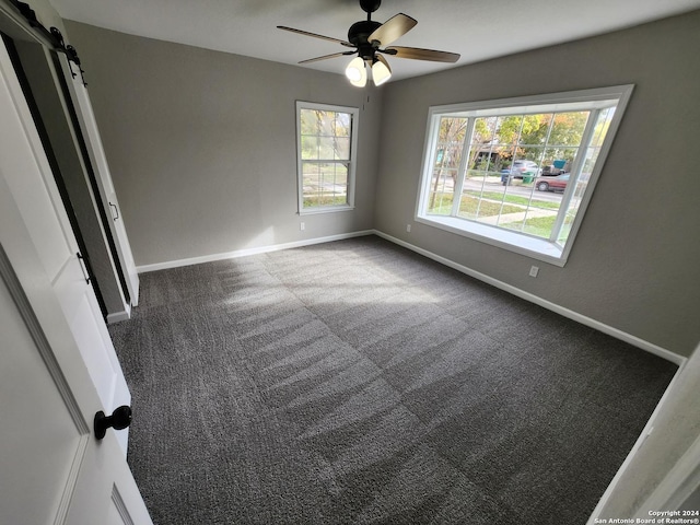 empty room with ceiling fan, a barn door, plenty of natural light, and dark carpet