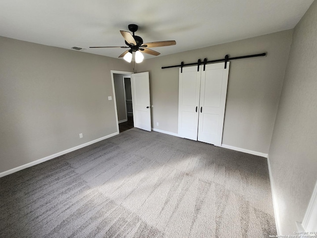 unfurnished bedroom with ceiling fan, a barn door, and dark colored carpet