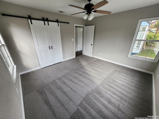 unfurnished bedroom with ceiling fan, a closet, a barn door, and dark colored carpet