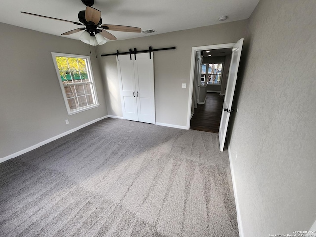 unfurnished bedroom featuring carpet flooring, ceiling fan, and a barn door