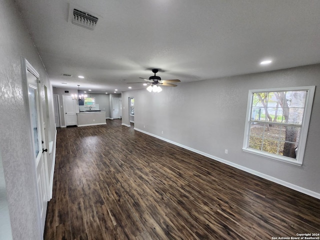 unfurnished living room with ceiling fan with notable chandelier and dark wood-type flooring