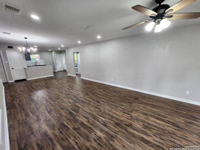 unfurnished living room featuring ceiling fan with notable chandelier, a textured ceiling, and dark hardwood / wood-style floors