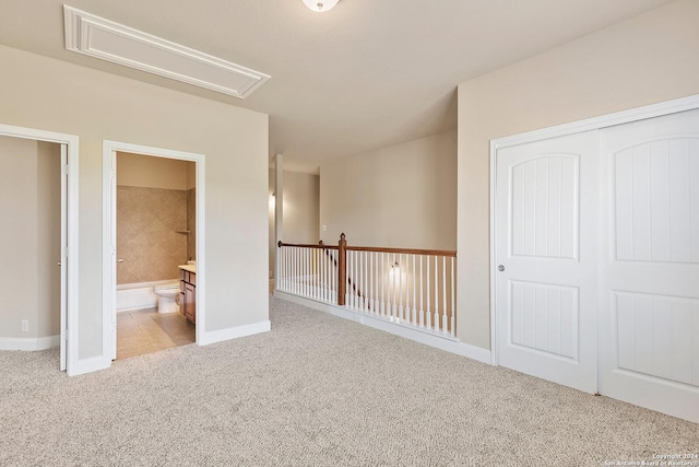 unfurnished bedroom with ensuite bathroom, light carpet, and a closet