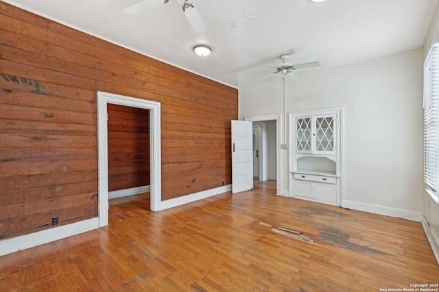 unfurnished bedroom featuring a closet, ceiling fan, hardwood / wood-style floors, and wood walls