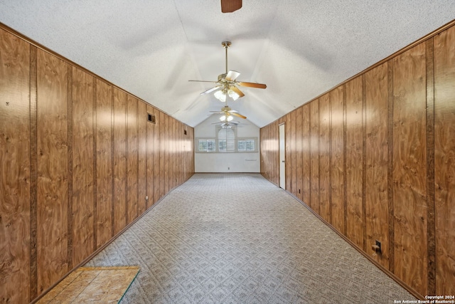 bonus room featuring wood walls, lofted ceiling, light carpet, ceiling fan, and a textured ceiling