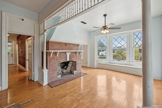 unfurnished living room featuring light wood-type flooring, ornate columns, ceiling fan, wooden walls, and a fireplace