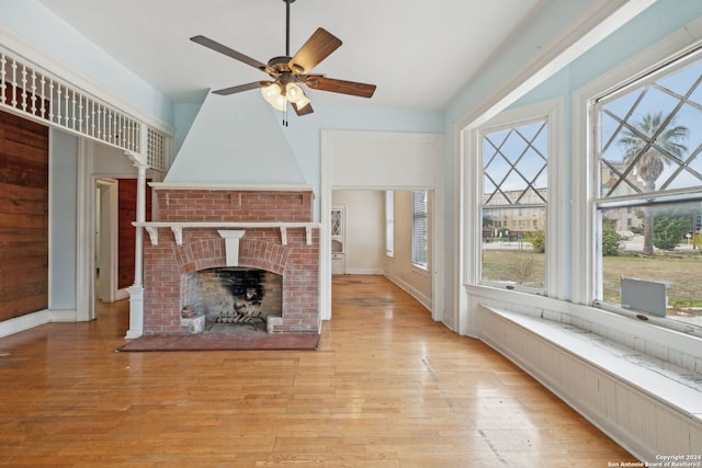 unfurnished living room featuring a brick fireplace, ceiling fan, a healthy amount of sunlight, and light hardwood / wood-style flooring