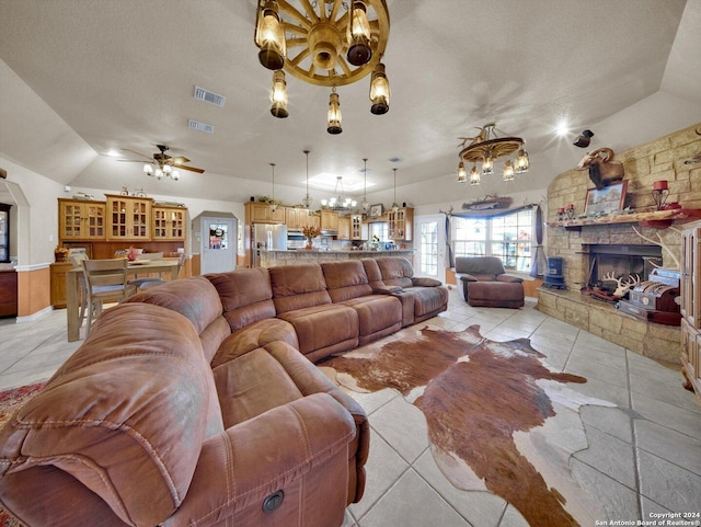 living room with ceiling fan with notable chandelier, a stone fireplace, light tile patterned floors, and a textured ceiling