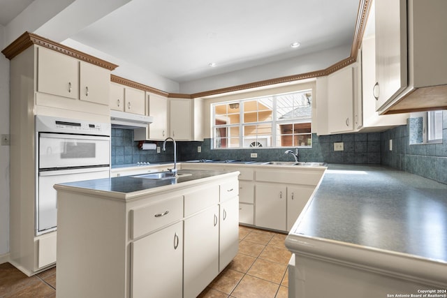 kitchen featuring a kitchen island with sink, sink, decorative backsplash, light tile patterned flooring, and white cabinetry