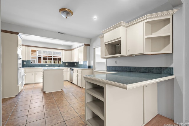 kitchen featuring kitchen peninsula, tasteful backsplash, stainless steel dishwasher, a center island, and white cabinetry