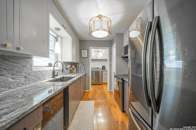 kitchen featuring appliances with stainless steel finishes, light wood-type flooring, backsplash, sink, and pendant lighting