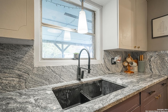 kitchen featuring tasteful backsplash, light stone countertops, sink, and pendant lighting