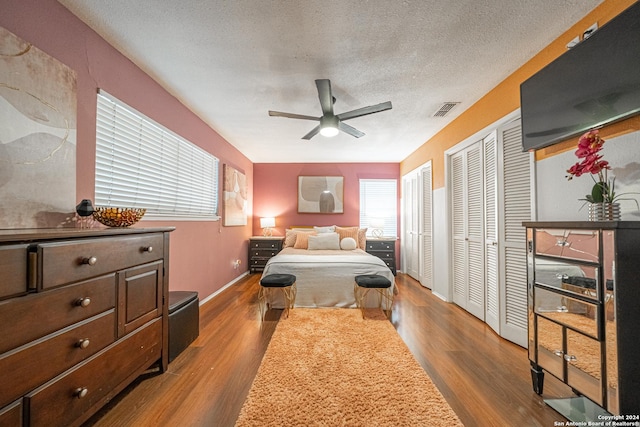 bedroom with multiple closets, ceiling fan, hardwood / wood-style floors, and a textured ceiling