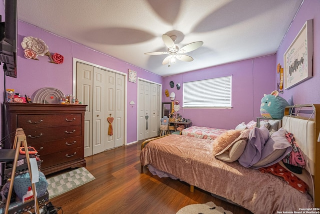 bedroom featuring a textured ceiling, ceiling fan, dark wood-type flooring, and two closets