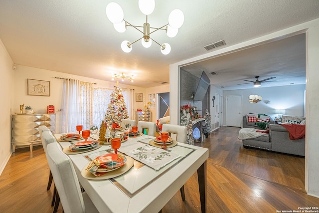 dining room featuring hardwood / wood-style flooring, ceiling fan with notable chandelier, and a textured ceiling