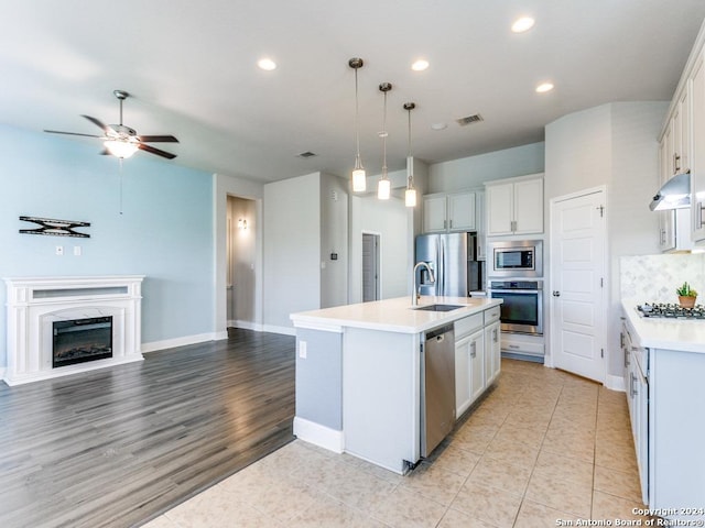 kitchen with a kitchen island with sink, white cabinets, sink, hanging light fixtures, and stainless steel appliances