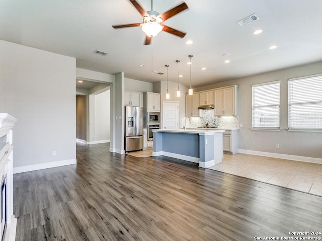 kitchen with backsplash, a center island with sink, hanging light fixtures, hardwood / wood-style flooring, and stainless steel appliances