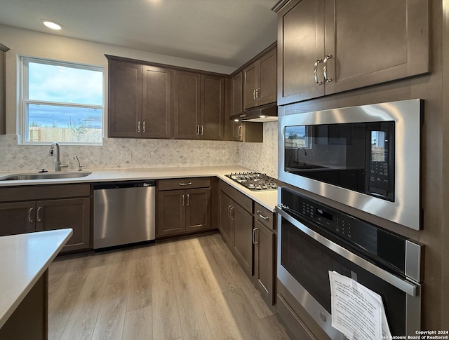 kitchen featuring sink, light wood-type flooring, appliances with stainless steel finishes, tasteful backsplash, and dark brown cabinetry