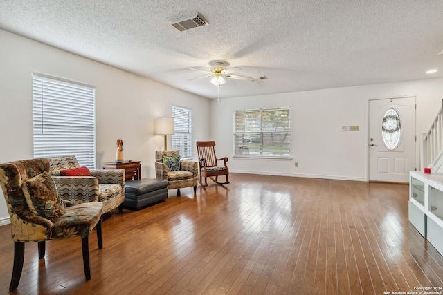 living area featuring visible vents, a ceiling fan, hardwood / wood-style floors, stairs, and a textured ceiling