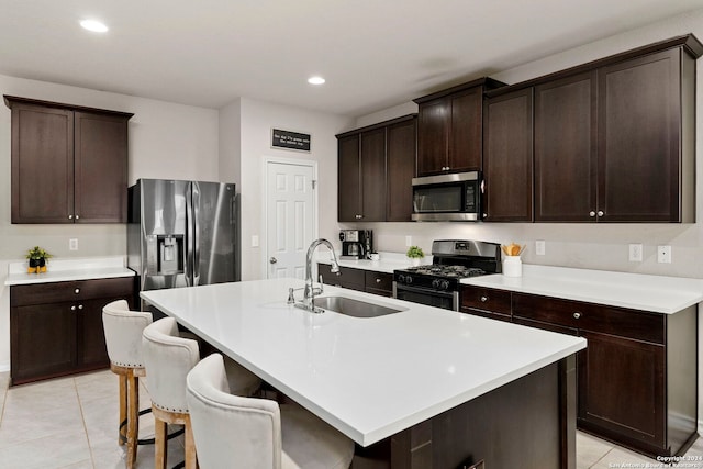 kitchen with light tile patterned floors, sink, appliances with stainless steel finishes, and an island with sink