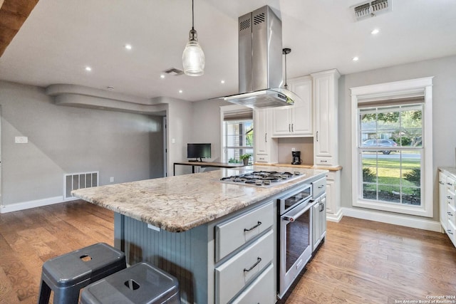 kitchen with a kitchen island, light wood-type flooring, island range hood, white cabinetry, and stainless steel appliances