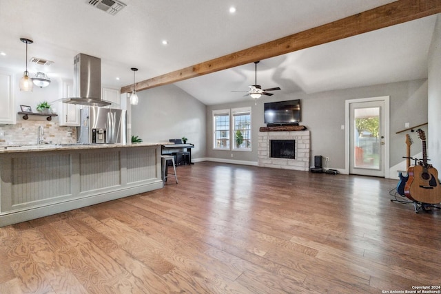 kitchen with white cabinetry, wall chimney range hood, stainless steel fridge with ice dispenser, decorative light fixtures, and a breakfast bar