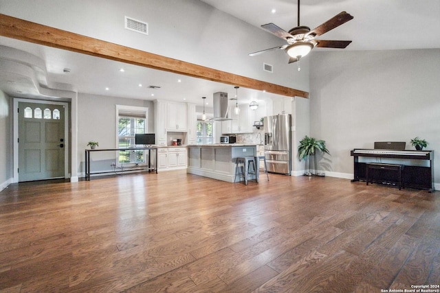 unfurnished living room with hardwood / wood-style floors, vaulted ceiling with beams, and ceiling fan