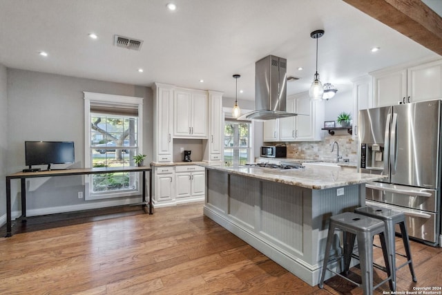 kitchen with light stone countertops, stainless steel appliances, island range hood, a healthy amount of sunlight, and white cabinets