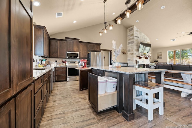 kitchen with a breakfast bar, a center island, light stone countertops, light wood-type flooring, and stainless steel appliances