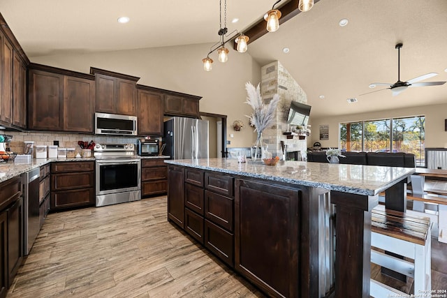 kitchen with dark brown cabinetry, stainless steel appliances, high vaulted ceiling, and a breakfast bar area